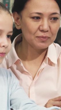 Neşeli küçük bir Asyalı kız ve şefkatli annesi renkli kitaplarla dolu samimi bir kütüphanede gülümseme ve meraklarını paylaşarak çevrimiçi bir öğrenme seansına daldılar. Bu yürek ısıtan an aşkın ve aşkın bağını güzel bir şekilde gösteriyor.