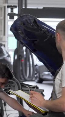 Alet ve araçlarla dolu canlı bir garajda, kendini adamış iki tamirci bozuk bir otomobili tamir etmek için odaklanmış bir diyaloğa giriyorlar. Bir erkek teknisyen, asistanı motoru incelerken not defterine titizlikle not alıyor.