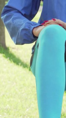 Göze çarpan mavi ceketli, odaklanmış atletik bir kadın, kulaklıklarını takmış, güneşli bir parkın canlı yeşillikleri arasında sabah antrenmanını yapmaya hazır. Canlandırıcı atmosfer motivasyon ve canlılık yayıyor.