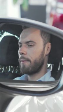 Işıldayan bir adam, şık arabasının ışıldayan yan aynasında arabanın anahtarlarını tutarken neşe saçıyor. Bu kendine güvenen genç işadamı, lüks araçlarla dolu modern bir sergi salonu ile çevrelenmiş başarı ve memnuniyeti temsil ediyor.