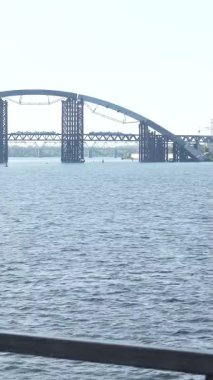 Büyüleyici bir nehir kenarı sahnesinde uzun siyah saçlı, at kuyruklu ve boynunu havluyla silen genç bir kadın var. Düşünceli bir şekilde ışıldayan suya ve şehir siluetine bakıyor. Huzurlu bir rahatlama anını ve doğayla olan bağlantısını somutlaştırıyor.