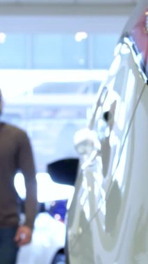 Zarif bir Afrikalı Amerikalı genç adam, otomotiv keşiflerinin heyecanını somutlaştırarak, bayiliğin modern bir kesişimine adım atıyor. Dinamik sahne, onu parlak araba kapısını açarken yakalıyor. Canlı bayilik ışıkları yansıtıyor.