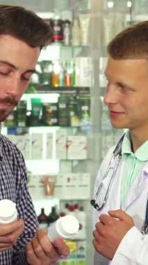 Aydınlık ve davetkar bir eczanede, beyaz önlüklü bir erkek doktor iki ilaç şişesini düşünceli bir şekilde karşılaştıran bir hastayla karşılaşır. Sahne profesyonellik ve samimiyet yayarak, bilgilendirilmiş kararların hayati önemini vurguluyor