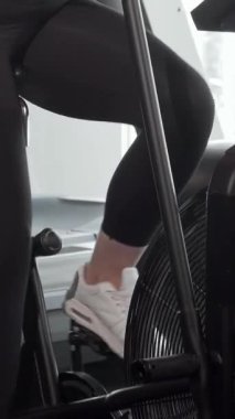 Kendine güvenen kıvrımlı bir kadın, spor salonundaki hava bisikleti üzerinde güçlü bir şekilde pedal çevirirken, spor yapmaya olan bağlılığını gösteriyor. Parlak, modern uzay, doğal ışıkla dolu, enerjisini ve vücudunun pozitifliğini arttırıyor, başkalarına ilham veriyor.