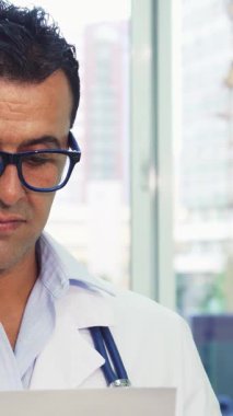 Şık gözlüklü neşeli bir doktor, önemli bir belgeyi incelerken kendine güveni tam bir onay veriyor. Geniş pencerelerden gelen doğal ışıkla yıkanan parlak ofisi profesyonellik ve sıcaklık yayarak davetkar bir atmosfer yaratıyor.