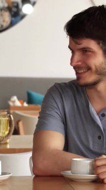 Sıcak ahşap aksanlar ve renkli yastıklarla süslenmiş şık bir kafede yakışıklı beyaz bir adam ve çarpıcı bir Asyalı kadın neşeli bir sohbete girişiyor. Gülüşleri neşe ve bağlantı yayıyor. Davetkar atmosfer gençlerle dolup taşıyor