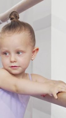 Leylak desenli taytlı, sevimli bir balerin kız bale barında bacağını zarifçe esnetiyor, neşe ve kararlılık saçıyor. Onun neşeli ifadesi ve zarif duruşu çocukluk hayallerinin büyüsünü ve dansın sanatsallığını somutlaştırıyor.