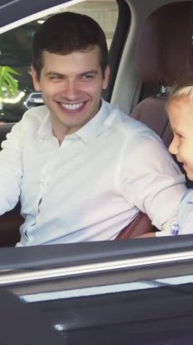 Gösterişli, modern bir aracın içinde, keyifli bir baba, büyüleyici bir menekşe elbise giyen meraklı kızının arabasının özelliklerini canlandırıyor. Paylaştıkları gülücükler ve ilgi çekici jestler aile bağlarının ve merakın iç açıcı bir tablosunu oluşturuyor.