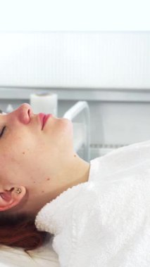 El değmemiş beyaz önlüklü yetenekli bir kozmetik uzmanı genç bir kadının yüzündeki ultrasonik makineyi ustalıkla çalıştırarak doğal güzelliğini arttırıyor. Huzurlu spa atmosferi müşteriler tarafından zenginleştirilir. Parlak cilt, güzellik uzmanı olarak.