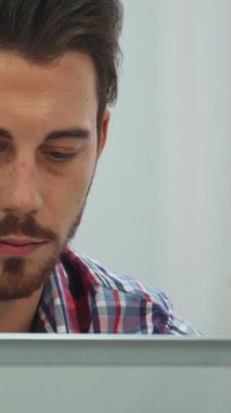 Koyu renk saçlı ve düzgün kesilmiş sakallı kendini adamış genç bir adam, yoğun bir şekilde dizüstü bilgisayarında daktilo ediyor, içi doğal ışık dolu parlak bir sınıfa daldırılmış. Sıcak güneş ışığı pencereden süzülüp, kareli gömleğine parıldıyor.