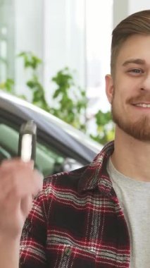 Düzgün bakımlı sakallı şık bir genç adam araba anahtarlarını gösterişli, modern bir galeride gururla sergilerken neşe saçıyor. Arkasındaki parıldayan araç yeni sahipliğin heyecanını simgeliyor, otomotiv hayallerinin özünü yakalıyor ve...