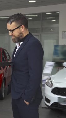 Gösterişli, modern bir araba galerisinde, kendine güvenen siyah takım elbiseli bir satış müdürü, sözleşmenin detaylarını tutkuyla genç beyaz bir müşteriye anlatıyor. Dinamik etkileşim yöneticiler tarafından vurgulanır, şık bir stile doğru jestler yaparlar.