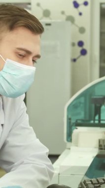 Pürüzsüz, modern bir laboratuvarda, üzerinde beyaz önlük ve koruyucu maske olan odaklanmış genç bir laboratuvar asistanı bilgisayarındaki test sonuçlarını özenle gözden geçirir. Eldivenli elleri klavyede zarifçe geziniyor, hassasiyetin özünü somutlaştırıyor.
