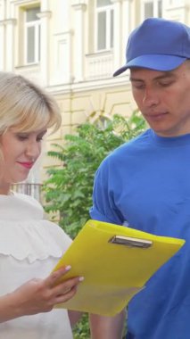 Mavi şapkalı, dost canlısı bir kuryeden karton bir paket alan, parlak sarı bir makbuzu imzalayan şık beyaz ışıklı neşeli bir kadın. Bu canlı açık hava sahnesi online alışverişin heyecanını yansıtıyor.