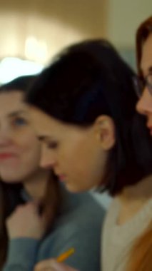 Çekici bir kız öğrenci, neşeli bir şekilde saçlarına dokunuyor. Nişanlı sınıf arkadaşlarıyla dolu bir konferans salonunda kendine güven ve neşe saçıyor. Bu yakın plan onun ışıl ışıl gülüşünü ve etkileyici özelliklerini yakalıyor, canlı bir öğrenme zeminine karşı kurulmuş ve