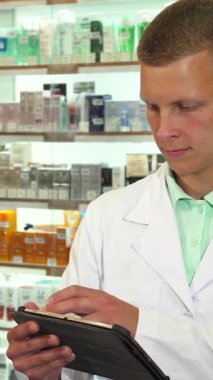 Gıcır gıcır beyaz önlüklü neşeli bir erkek eczacı şık bir tabletle etkileşime girer. Sıcak gülümsemesi canlı eczane arkaplanını aydınlatır. Renkli sağlık ürünlerinin düzenli raflarıyla çevrelenmiş, profesyonelliği ve...