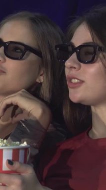 Sıcak bir sinema salonunda, üç boyutlu gözlüklerle süslenmiş iki genç kadın heyecan verici bir film hakkındaki düşüncelerini tutkuyla paylaşıyorlar. Aralarına yerleştirilmiş çizgili bir patlamış mısır kovası ile kahkahaları ve heyecanları sahneyi aydınlatıyor.