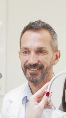 Keyifli bir dişçi gururla ışıldar. Hastası, dişlerindeki başarıyı yansıtan parlak bir aynada onun göz kamaştırıcı gülümsemesine hayran kalır. Bu iç açıcı an modern diş bakımında bulunan güven ve memnuniyeti özetliyor.