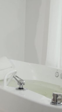 Işıl ışıl gülümseyen neşeli bir kadın lüks bir girdap banyosuna adım atıyor ve rahatlatıcı bir hidromasaj yaptırmaya hazır. Camdan süzülen yumuşak doğal ışıkla aydınlatılan sakin spa ortamı, davetkar bir davet yaratıyor.