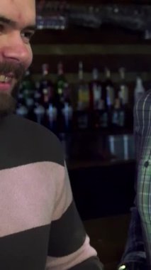 Animasyon tebessümlü üç neşeli Kafkasyalı arkadaş hareketli bir barda neşeli bir tostla bira bardaklarını kaldırıyor. Yakın plan, bulaşıcı kahkahalarını ve arka planda renkli şişelerle dolu canlı ambiyanslarını yakalıyor.