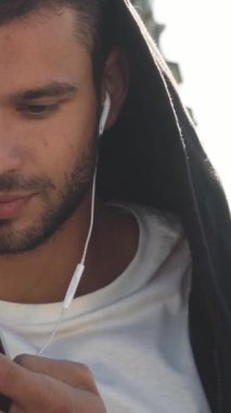 Koyu saçlı ve bakımlı sakallı neşeli bir genç adam bir bankta oturuyor, telefonuyla meşgul bir şekilde mesajlarına cevap veriyor. Onun ışıltılı gülümsemesi canlı bir şehir zemininde parıldıyor, şehrin canlı enerjisini yakalıyor.