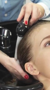 Parlak tenli neşeli genç bir kadının yakın plan çekimi yetenekli bir kuaförün, parlak siyah bir leğenle kafa derisine nazikçe masaj yapması gibi rahatlatıcı bir saç yıkamasının tadını çıkarıyor. Bu huzurlu an, kendine bakmanın lüksünü simgeliyor. Şımartma sanatını sergiliyor.