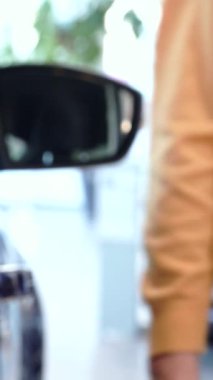 Üst düzey bir beyaz adam, canlı bir galeride yeni arabaların arka kapılarını hevesle sergiliyor. Eli nazikçe çarpıcı mor bir geçitin kapısını kapatıyor, yeni araba sahibi olmanın heyecanını ve canlı bir atmosferi yayıyor.