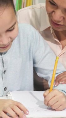 Samimi bir kütüphanede, sevimli küçük bir kız not defterine yazdığı gibi sevinçle ışıldarken özenli annesi nazik bir rehberlik sunuyor. Bu dokunaklı öğrenme anı aile bağlarının sıcaklığını ve eğitimin neşesini özetliyor.