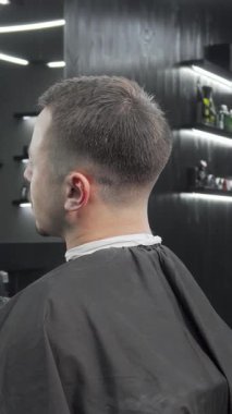 Gösterişli, modern bir berber dükkanında, yetenekli bir berber, erkek müşterisi için bir ayna tutar, o da taze ve şık saç kesiminden memnuniyet duyar. Titreşimli atmosfer, her ayrıntının katkı sağladığı tımarcılığın sanatsallığını vurguluyor.