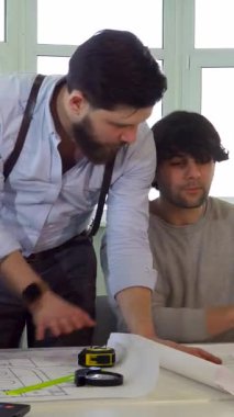 Kendini işine adamış genç beyaz bir mimar, entrika dolu çalışma arkadaşlarıyla modern ofis masasında karmaşık proje planlarını tartışıyor. Planlar, dizüstü bilgisayar ve başlıkla çevrelenmiş bu canlı sahne işbirliği ve kıvılcımlar saçar.