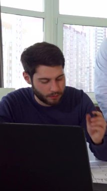 Kendini işine adamış genç beyaz bir mimar parlak ve modern bir ofiste nişanlısına karmaşık proje planlarını tutkuyla sunuyor. Şablonlar, parlak bir dizüstü bilgisayar ve sağlam bir şapkayla çevrelenmiş sahne, işbirliği ve yaratıcılık yayıyor.