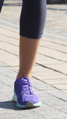 Açık tenli genç bir kadın, güzel bir nehir yürüyüşünde bacaklarını enerjik bir şekilde açar ve güneşin altında güneşlenir. Şık mor spor ayakkabılar giyip, tozluklarını giyerek, canlılık ve zarafeti somutlaştırıyor, parıldayan mavi suyla çevrili