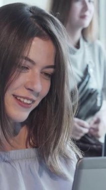 Hoş bir kafede dizüstü bilgisayarı üzerinde çalışırken canlı bir görüntülü konuşma yapan dalgalı saçlı çekici bir kadın ışıl ışıl gülümsüyor. Yumuşak doğal ışık ve sohbetin hafif uğultusuyla zenginleşen ılık ortam,