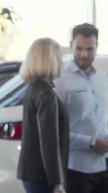 Neşeli bir çift, ışıldayan araçlar ve çarpan kırmızı bir fiyonk ile çevrili canlı bir araba galerisinde şık bir otomobili zevkle inceliyor. İfadeleri heyecan ve heyecan saçar ve önlerindeki heyecanlı yolculukları hayal ederler.