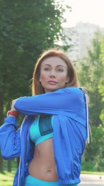 Zarif bir bayan sporcu, canlandırıcı koşusuna başlamak üzere yemyeşil bir parkta hazır bekliyor. Sıcak güneş ışığıyla yıkanmış, zindelik ve güç yayıyor, şık ve enerjik spor kıyafetleriyle kendini spora adadığını gösteriyor.