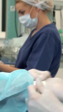 Odaklanmış bir cerrahi ortamda, kendini işine adamış bir hemşire doktorların eline dikkatlice sterilize bir eldiven takarak güvenliği ve hijyeni ön plana çıkarıyor. Bu samimi an cerrahi ekibinin hasta bakımına olan sarsılmaz bağlılığını gözler önüne seriyor.