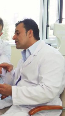 Güneşli bir muayenehanede, beyaz önlüklü iki erkek doktor X-Ray görüntülerini titizlikle incelerken, odaklanmış bir tartışmada genç bir kadın beklentiyle sonuçlarını bekliyor. Bu sahne adanmışlığı güzel bir şekilde gösteriyor.