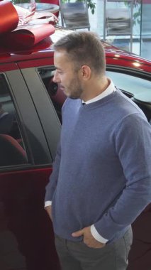 Gösterişli araçlarla dolu modern bir araba galerisinde, rahat bir süveter giyen şık bir satıcı, nişanlı bir alıcıya ışıldayan yeni arabanın etkileyici özelliklerini büyük bir hevesle sergiliyor. Alıcı, sakallı düşünceli bir adam, dikkatle dinler,