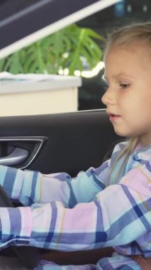 Uzun sarı saçlı neşeli küçük bir kız direksiyona sarılıp neşeli bir tebessümle anahtarlara uzanırken heyecanla parıldıyor. Renkli çizgili bir gömlek giymiş, coşkusu yayılıyor, izleyicileri hayal dünyasına davet ediyor.