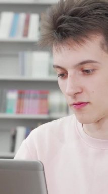 Canlı, kırpılmış bir karede, önünde parlak bir dizüstü bilgisayar bulunan canlı bir kütüphanede çalışmalarına derinden bağlı gülümseyen genç bir erkek öğrenci yer alıyor. Bulaşıcı gülümsemesi ve günlük kıyafetleri öğrenme tutkusunu yansıtıyor.