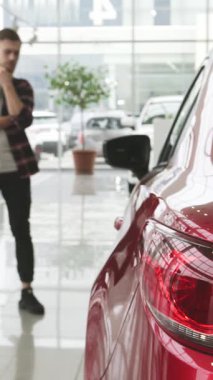 Sakallı bir adam şık bir araba galerisinde duruyor. Etrafı zarif otomobillerle çevrili parlak kırmızı bir araca dikkatlice bakıyor. Parlak, modern gösteri salonu heyecan ve heyecanla uğulduyor, tüketicinin özünü yakalıyor.