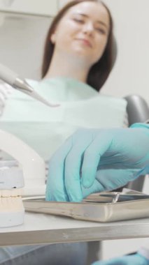 Canlı önlük giymiş odaklanmış bir erkek dişçi, ön planda detaylı diş kalıbı ve parıldayan aletlerle sakin bir kadın hastanın dişlerini titizlikle inceliyor. Bu parlak, modern klinik sahnesi profesyonelliği ve güveni gözler önüne seriyor.