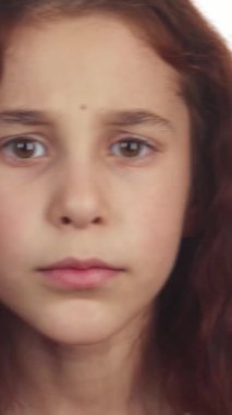 Bu sevimli kız, kıvırcık siyah saçları ile yüzünü çerçeveliyor, sessiz kalmak için parmağını dudaklarına dayayarak işaret veriyor. Geniş, anlamlı kahverengi gözleri, yumuşak beyaz arka plana karşı merakla parıldıyor, enfes ve çekici bir şey yaratıyor.