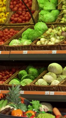 Genç beyaz bir adam, şık bir ekose gömlek giymiş, düşünceli bir şekilde canlı bir hipermarkette canlı kırmızı bir dolma biber ve gevrek yeşil bir lahana seçiyor. Odaklanmış tavrı, renkli bir yolda ilerlerken sağlıklı beslenmek için coşku yayıyor.