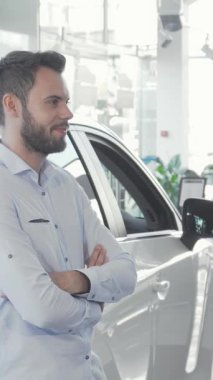 Kendine güvenen genç beyaz bir adam parlak, parlak yeni aracının yanında duruyor, elinde parlak bir gülümsemeyle arabanın anahtarlarını tutuyor. Parlak, modern galeri, arabanın üzerinde büyük kırmızı bir fiyonk ile süslenmiş, heyecan ve yeni sahiplik sevinci yayıyor, izleyicileri davet ediyor