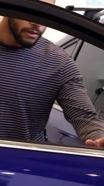 Şık, genç siyahi bir adam gösterişli, modern bir galeride çarpıcı bir mor geçidin kapısını coşkuyla açıyor. Işıl ışıl gülüşü ve coşkulu başparmakları yeni sahibi olmanın coşkulu anını yakalıyor, arabanın heyecanını gösteriyor.