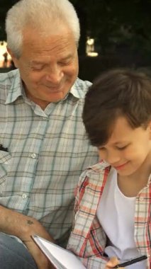 Küçük tatlı beyaz bir çocuk, büyük babasının değerli bilgeliğini yakalamak için hevesle defterine yazıyor. Parktaki bankta sıcak güneş ışığıyla yıkanan yakışıklı, gri saçlı emekliler gururla ışıldıyor. Dokunaklı bir bağ anı yaratıyor.