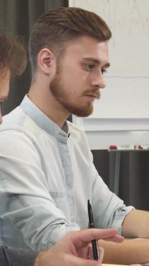 Şık sakallı neşeli genç bir adam, modern, güneşli bir ofisteki parlak bir dizüstü bilgisayarda tutkulu bir şekilde beyin fırtınası yapan olgun meslektaşına ışıldıyor. Bu canlı sahne yaratıcılığı ve takım çalışmasını yayıyor, ilham verici sinerjiyi vurguluyor.