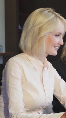 Gösterişli, modern bir ofiste, iki sarışın iş kadını parlak ahşap bir masada şık bir dizüstü bilgisayarın üzerine eğilmiş canlı bir tartışmaya dalmış durumdalar. Animasyon ifadeleri coşku ve işbirliği yayarak ilham verici bir atmosfer yaratıyor.