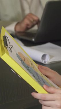 Uzun sarı saçlı, kendine güvenen bir iş kadınının canlı bir yakın çekimi. Zarif, modern bir ofiste renkli belgeleri incelerken neşeyle gülümsüyor. Atmosfer pozitiflik ve profesyonellik yayıyor, onun kendini adamışlığını ve başarısını vurguluyor